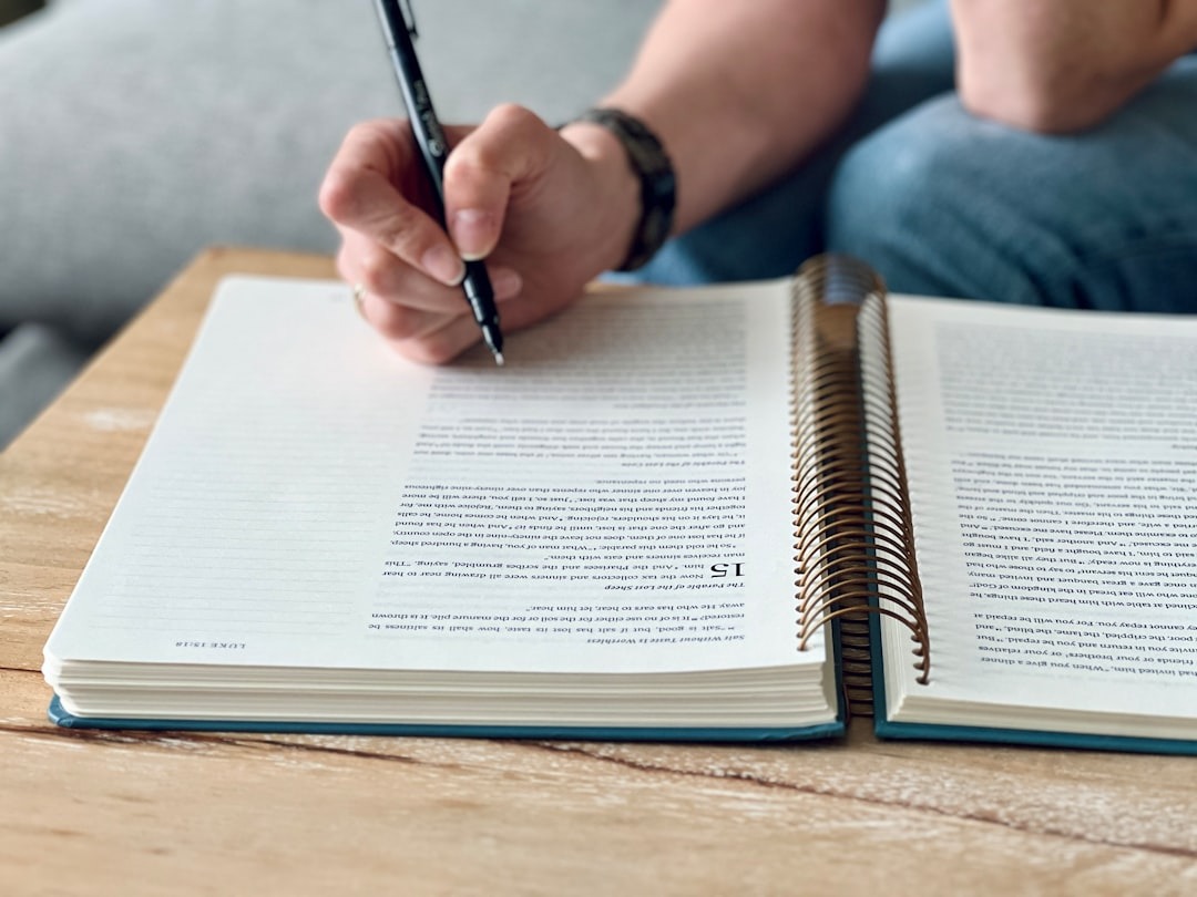Hand writing in a spiral notebook on a wooden table.