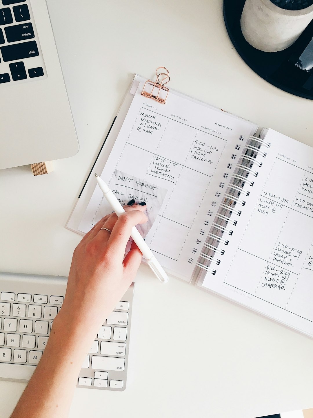 Hand writing in a weekly planner on a white desk.